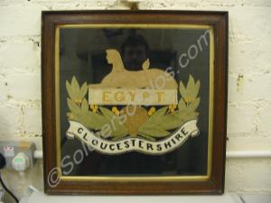 Framed embroidered pictures of regimental badges.