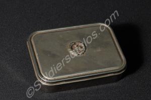 White metal tin with back badge on lid. Contained