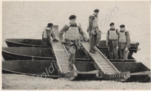 Two soldiers walking across pontoon boats. 1st Bat