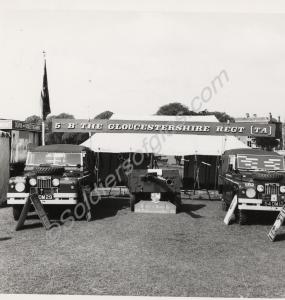 Land Rovers and A/T gun at a stand with a banner r